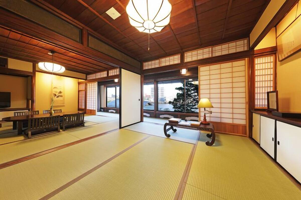 A traditional Japanese room with tatami flooring, a low table with benches, sliding doors, and a ceiling light fixture.