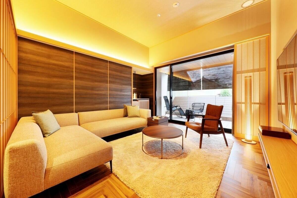 A modern living room with a sofa, coffee table, and chairs, large windows, and a flat-screen TV.