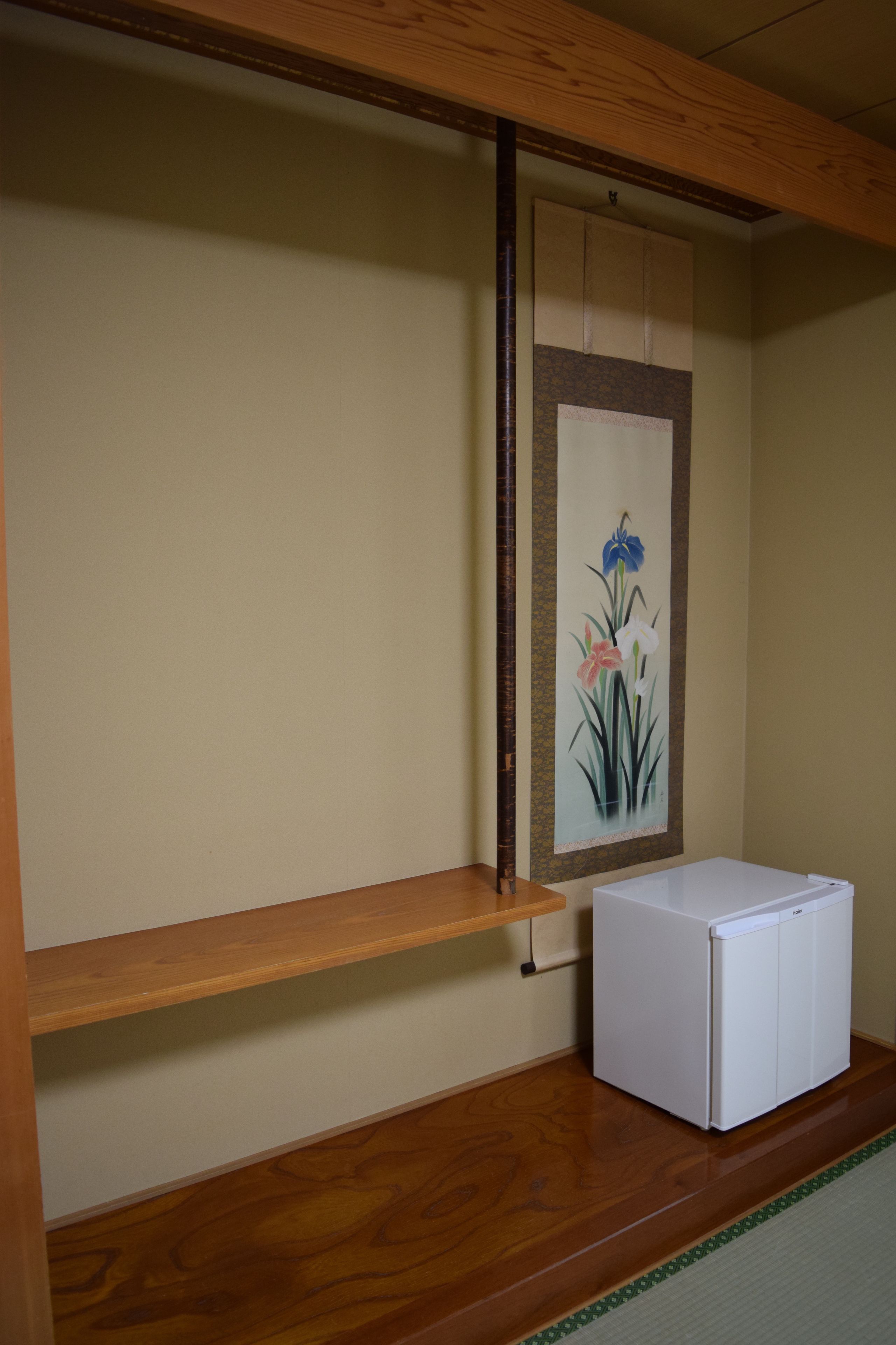 A room with a wooden beam ceiling, a white refrigerator, a wooden shelf, and a wall-mounted painting of flowers.