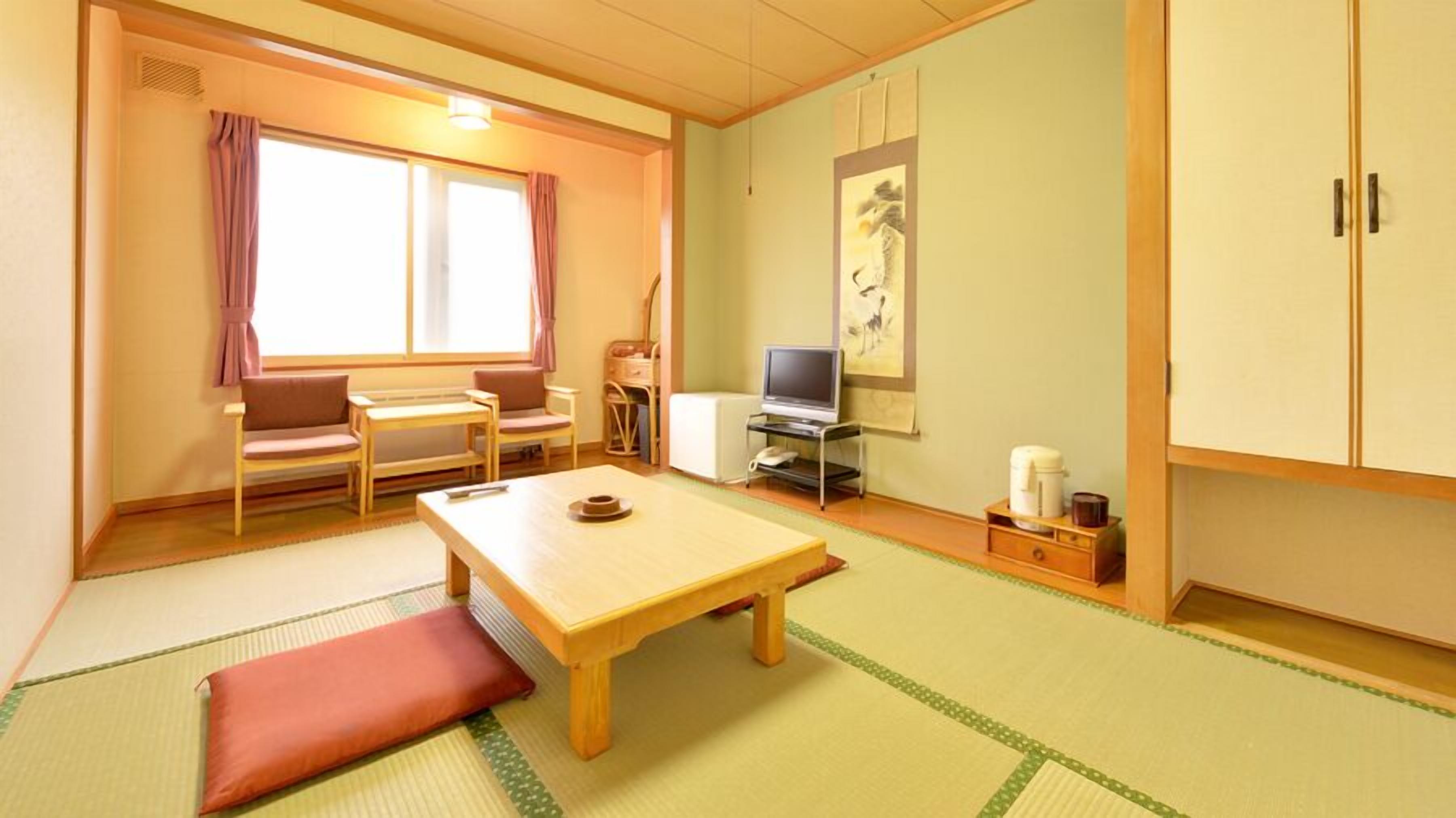 Una tradizionale stanza giapponese con pavimento in tatami, un tavolino, una poltrona, un televisore e un mobiletto.