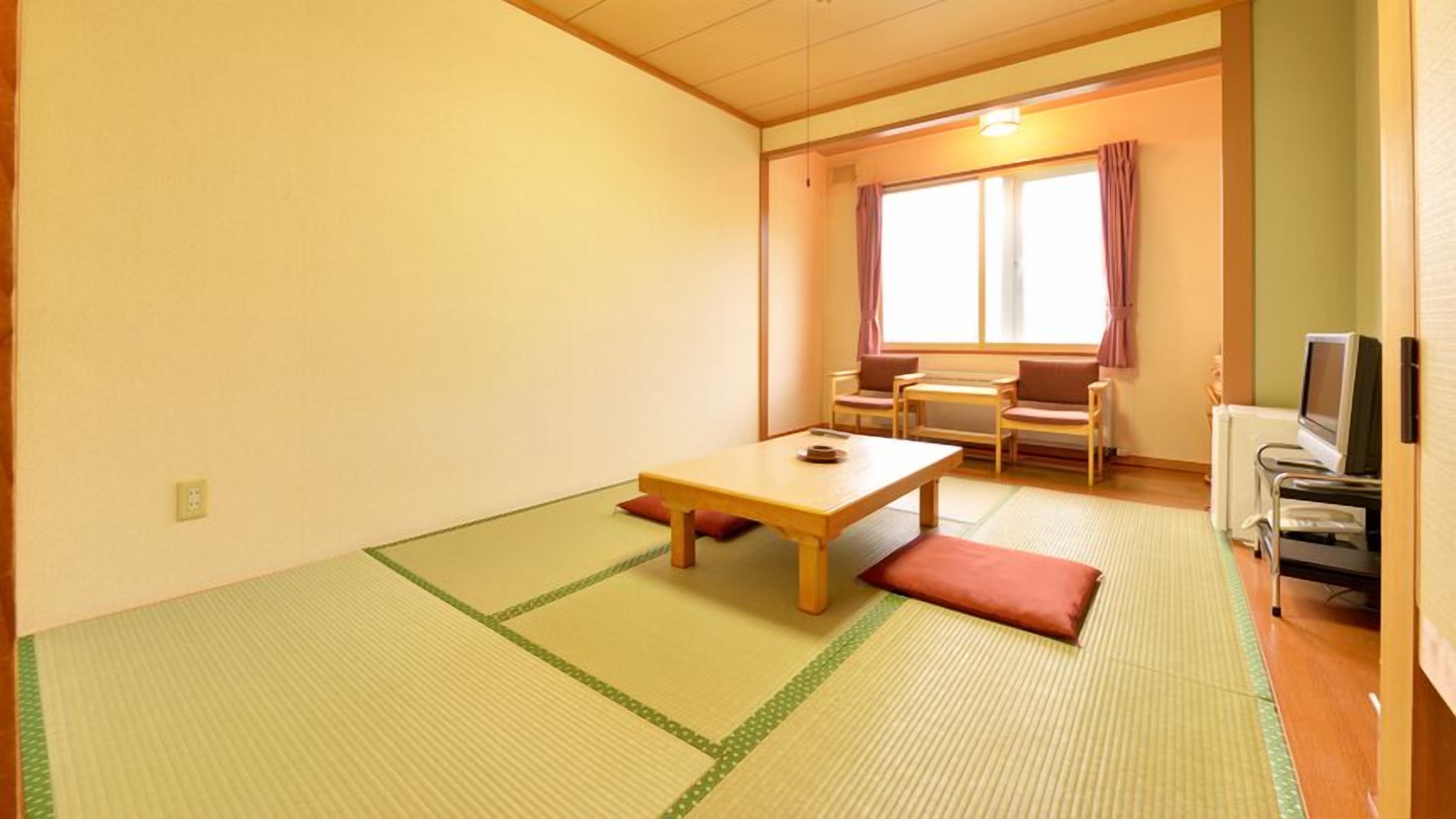 Una stanza con tatami, un tavolino, sedie, una TV e una finestra con tende.