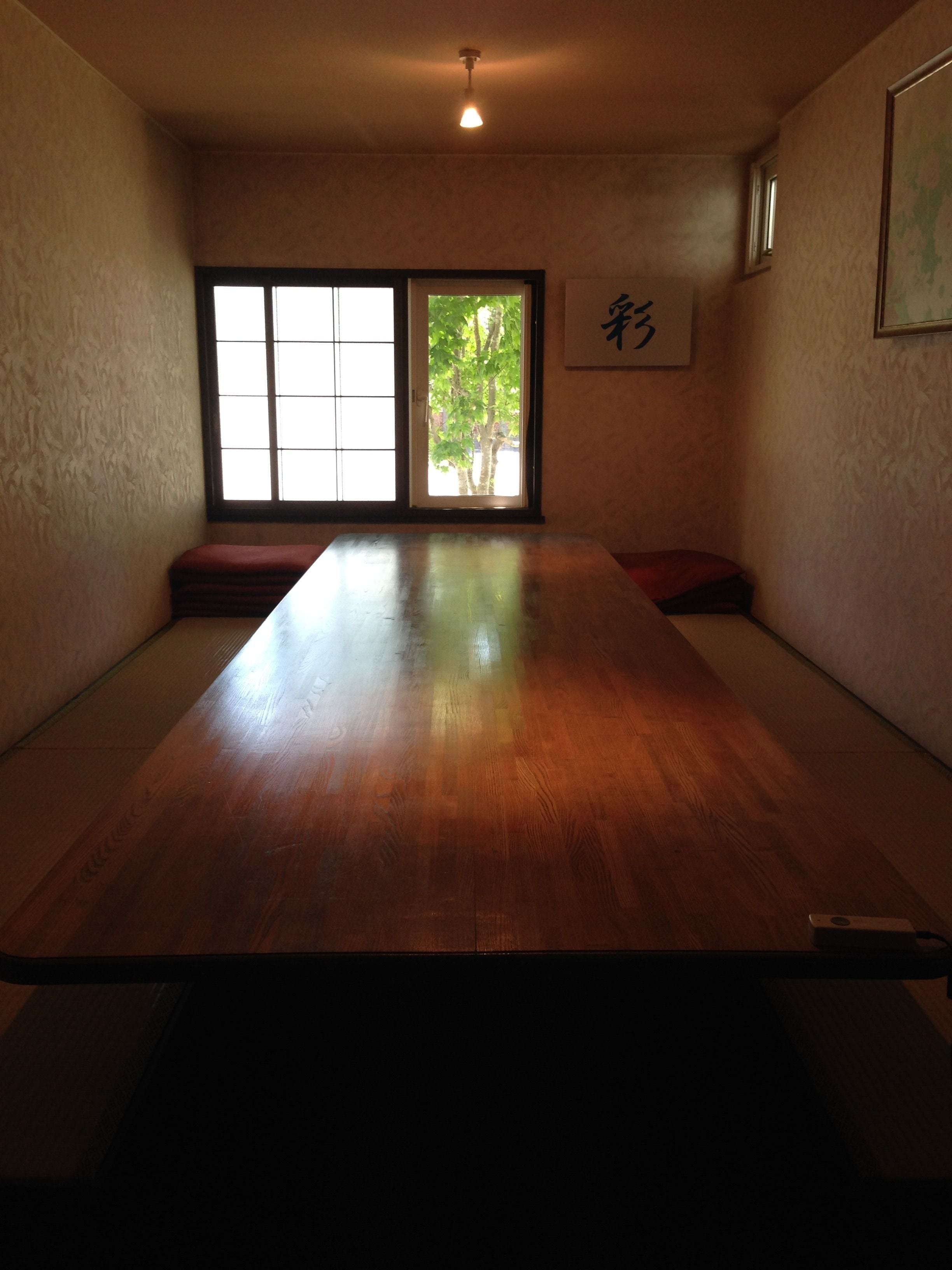 A traditional Japanese-style room with tatami flooring, a low wooden table, sliding doors, and a view of greenery outside.
