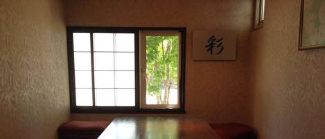 A traditional Japanese-style room with tatami flooring, a low wooden table, sliding doors, and a view of greenery outside.