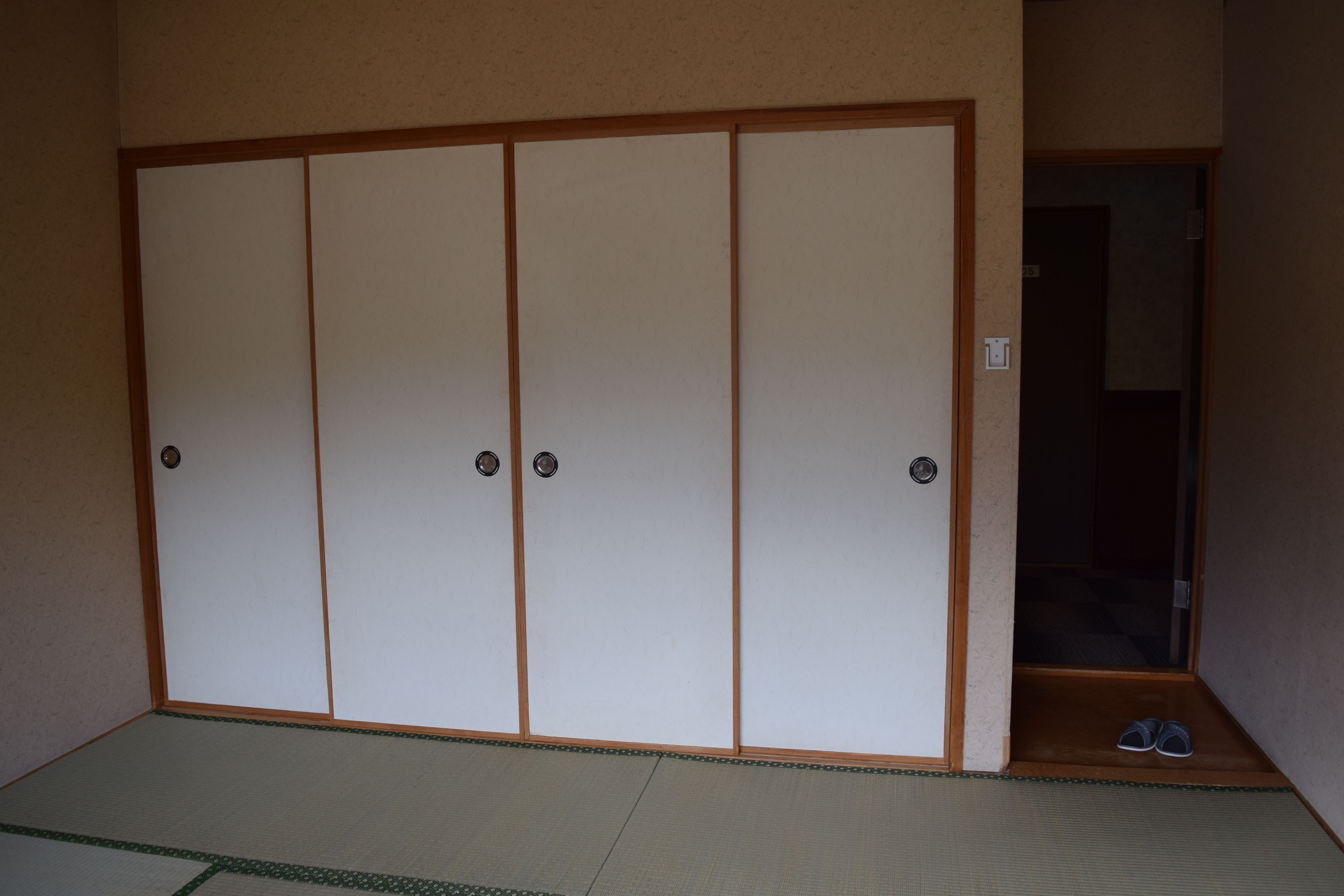 Une pièce de style japonais traditionnel, avec un sol recouvert de tatamis, une porte coulissante et une petite entrée où se trouvent une paire de chaussons.
