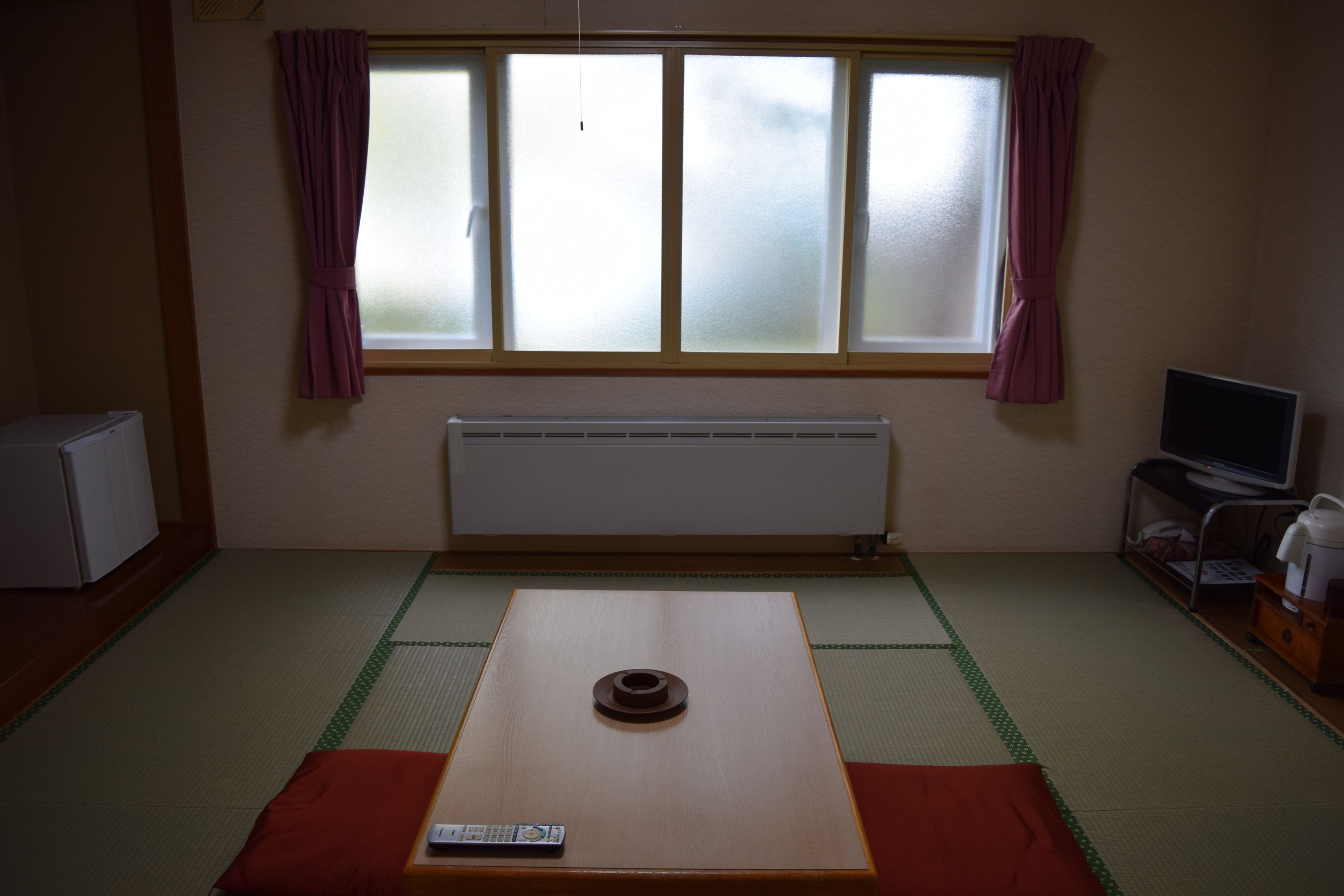 A room with tatami flooring, a futon bed, a television, and a small refrigerator.