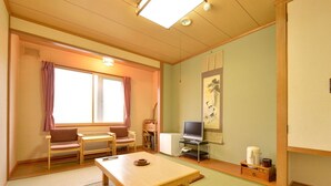 Una habitación japonesa tradicional con suelo de tatami, una mesa baja, un sofá, un televisor y un armario.