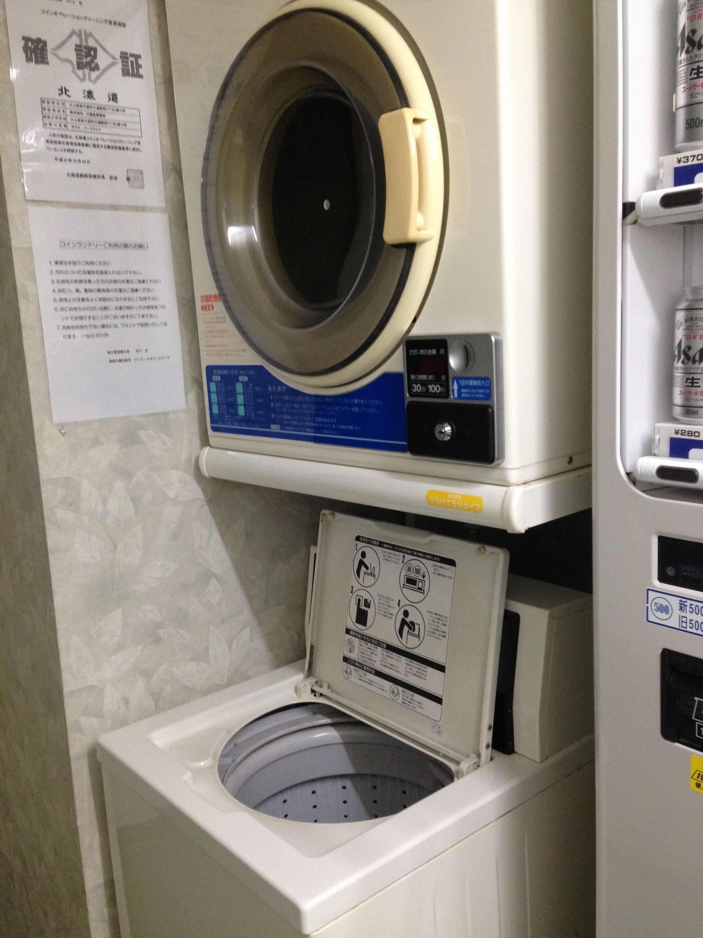 A front-loading washing machine with a control panel, a detergent dispenser, and a paper instruction manual on the wall.