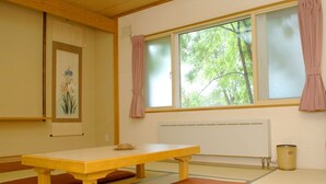Una habitación japonesa tradicional con suelo de tatami, una mesa baja, cojines, un radiador y una ventana con cortinas.