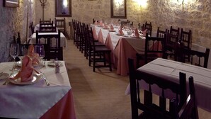 A long table set for dining in a stone-walled room with arched ceilings and framed pictures on the walls. - Señorio de Olmillos (Sasamon)
