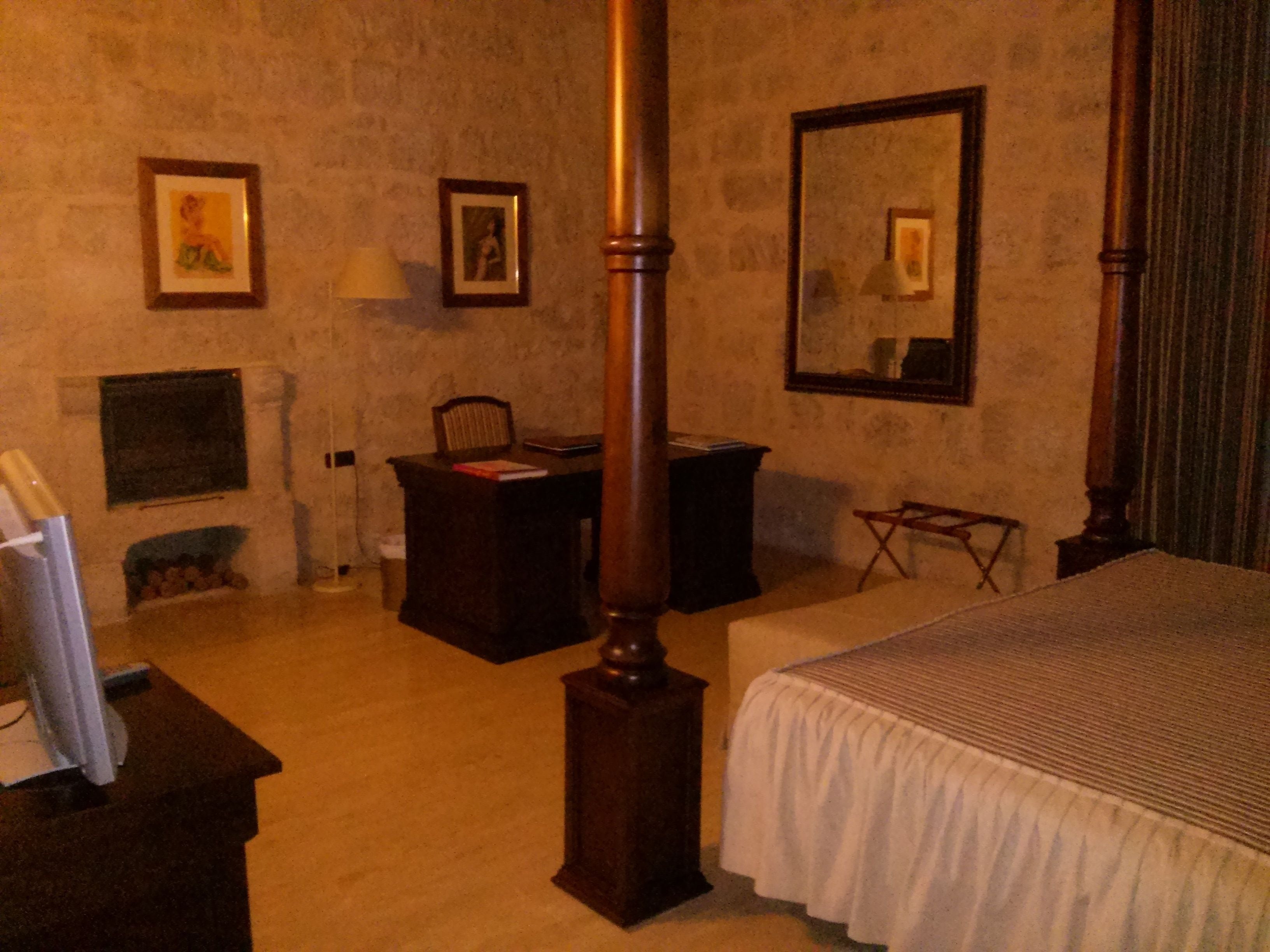 Una habitación con cama, escritorio, silla, chimenea y un espejo grande.