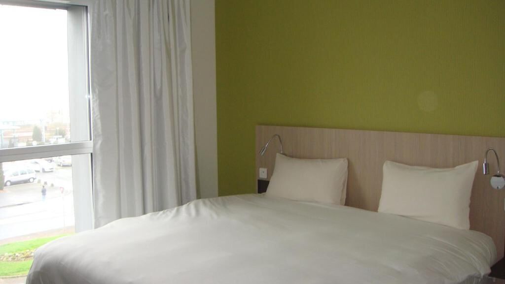 A hotel room with a large bed, a window with curtains, and a view of the outside.