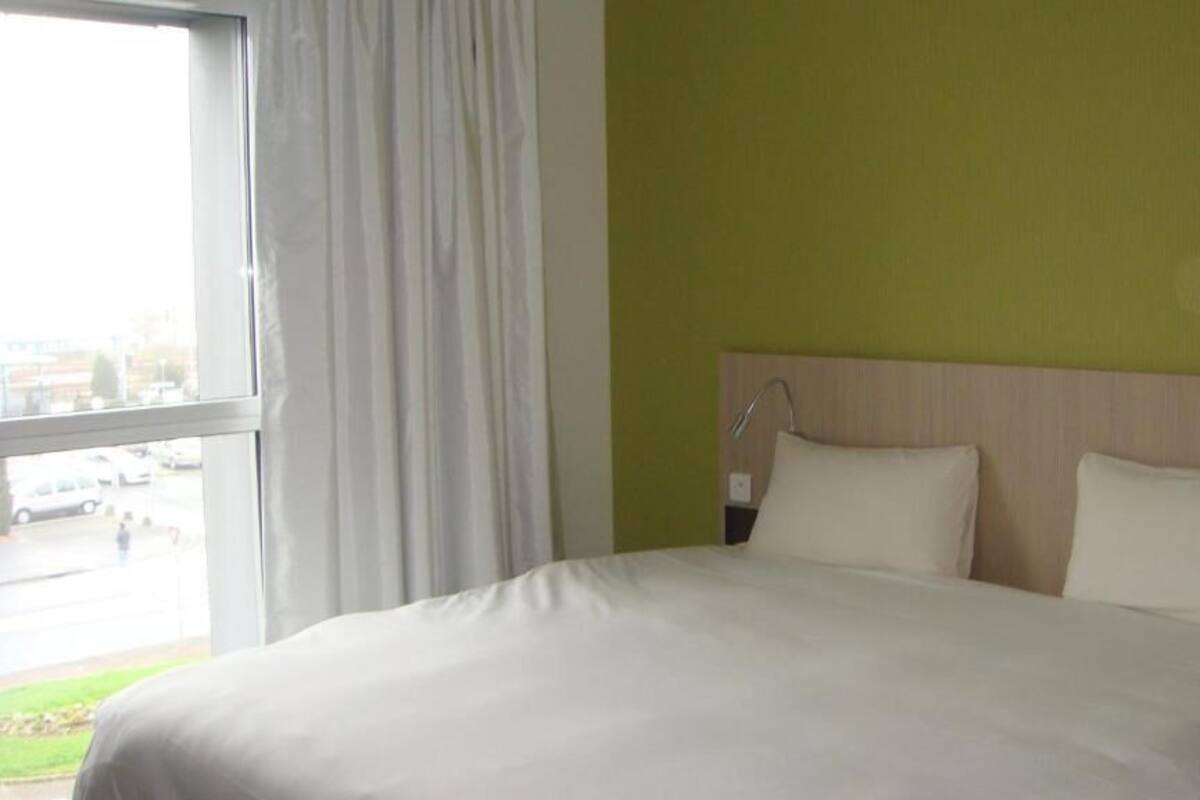 A hotel room with a large bed, a window with curtains, and a view of the outside.