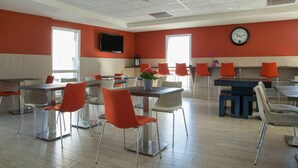 A dining area with tables and chairs, a clock on the wall, and a television mounted above a counter. - The Originals Access, Hôtel Cholet Gare (Cholet)