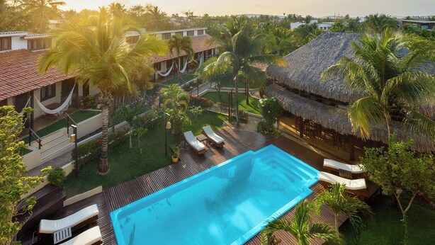 Un resort con piscina, sillas de descanso y estructuras de techo de paja.