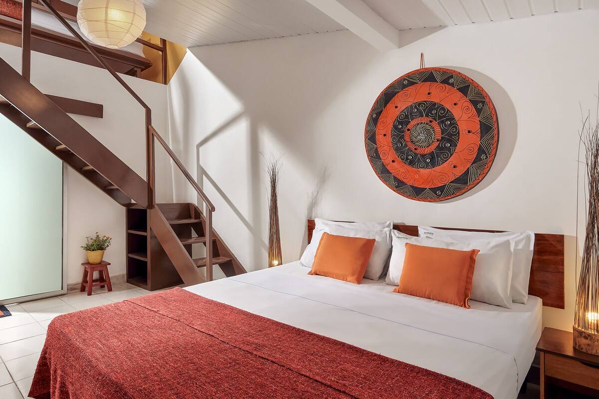 A bedroom with a large bed, a wooden staircase, and a wall-mounted circular artwork.