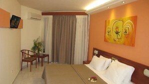 A hotel room with a bed, a chair, a small table, and a painting on the wall. - Miramare Bay Hotel (Karpathos)