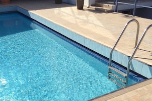Una piscina rectangular con agua azul cristalina, bordes azulejados y una escalera metálica a la derecha.