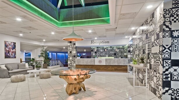 A modern reception area with a glass coffee table, a sofa, and a reception desk. - Miramare Bay Hotel (Karpathos)