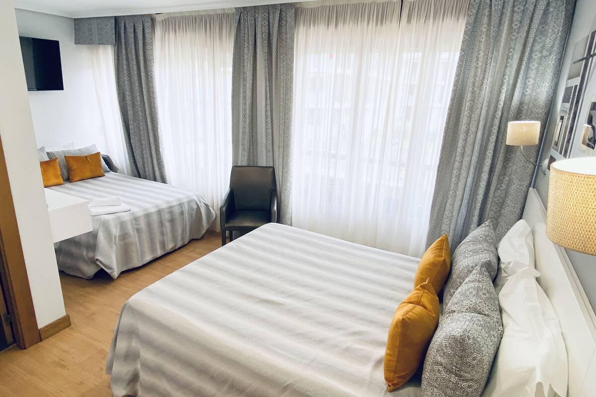 A hotel room with two beds, a chair, a TV, and a lamp.