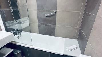Un baño moderno con ducha de vidrio, una bañera blanca y un inodoro.