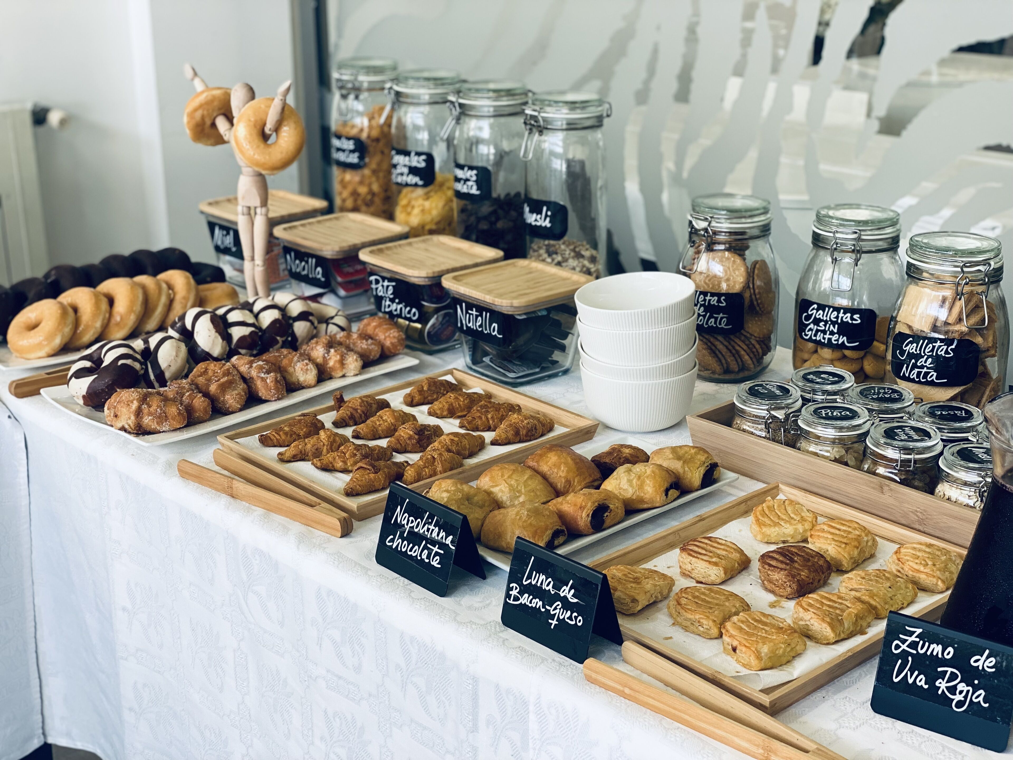 A bakery display with various pastries and baked goods, including croissants, donuts, and cookies, labeled with names like "Napolitana chocolate" and "Luna de Balam Gueso".