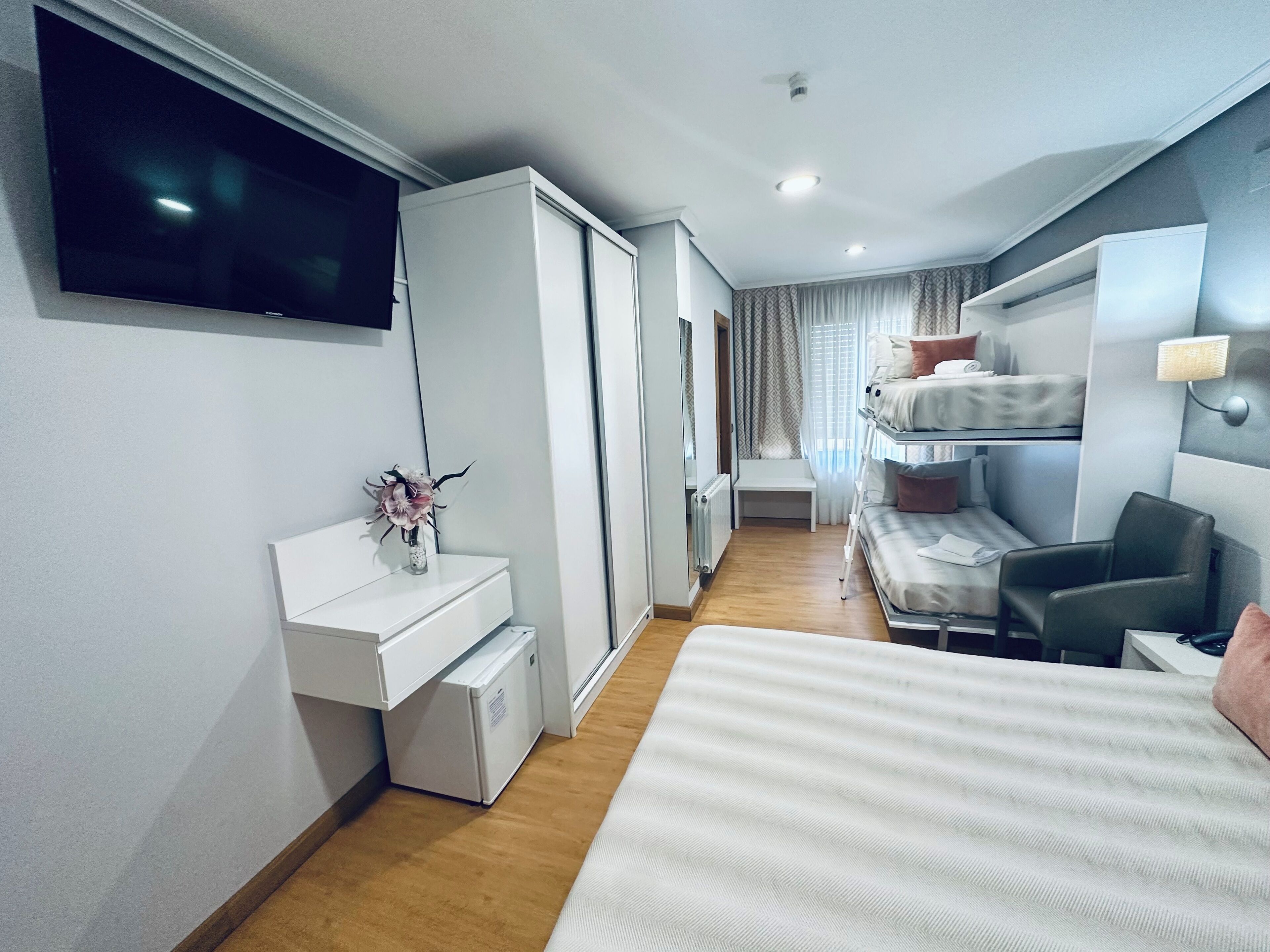 A hotel room with a bed, a desk, a chair, a TV, and a window with curtains.