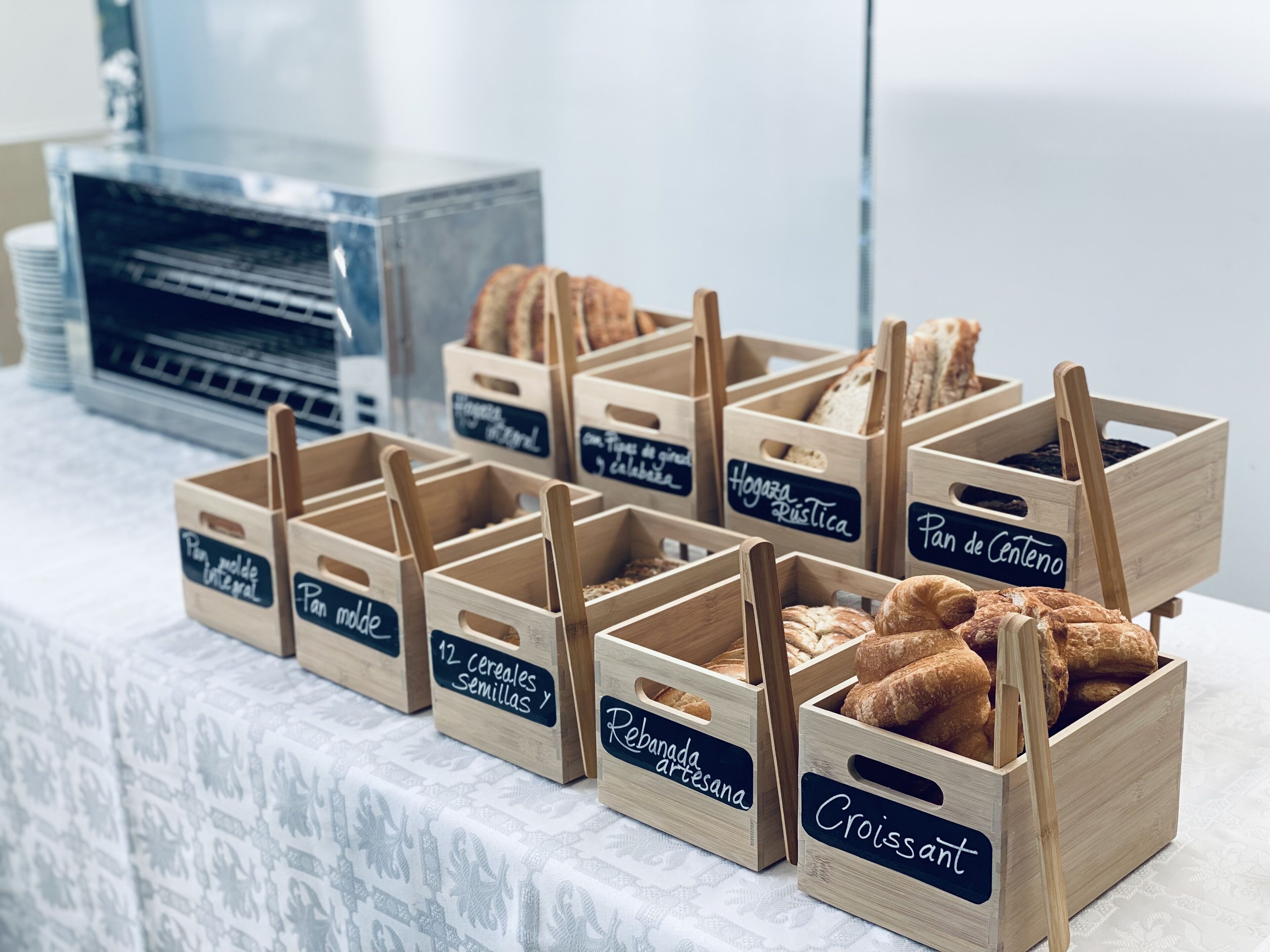 Cajas de madera etiquetadas con distintos tipos de pan y repostería sobre una mesa.