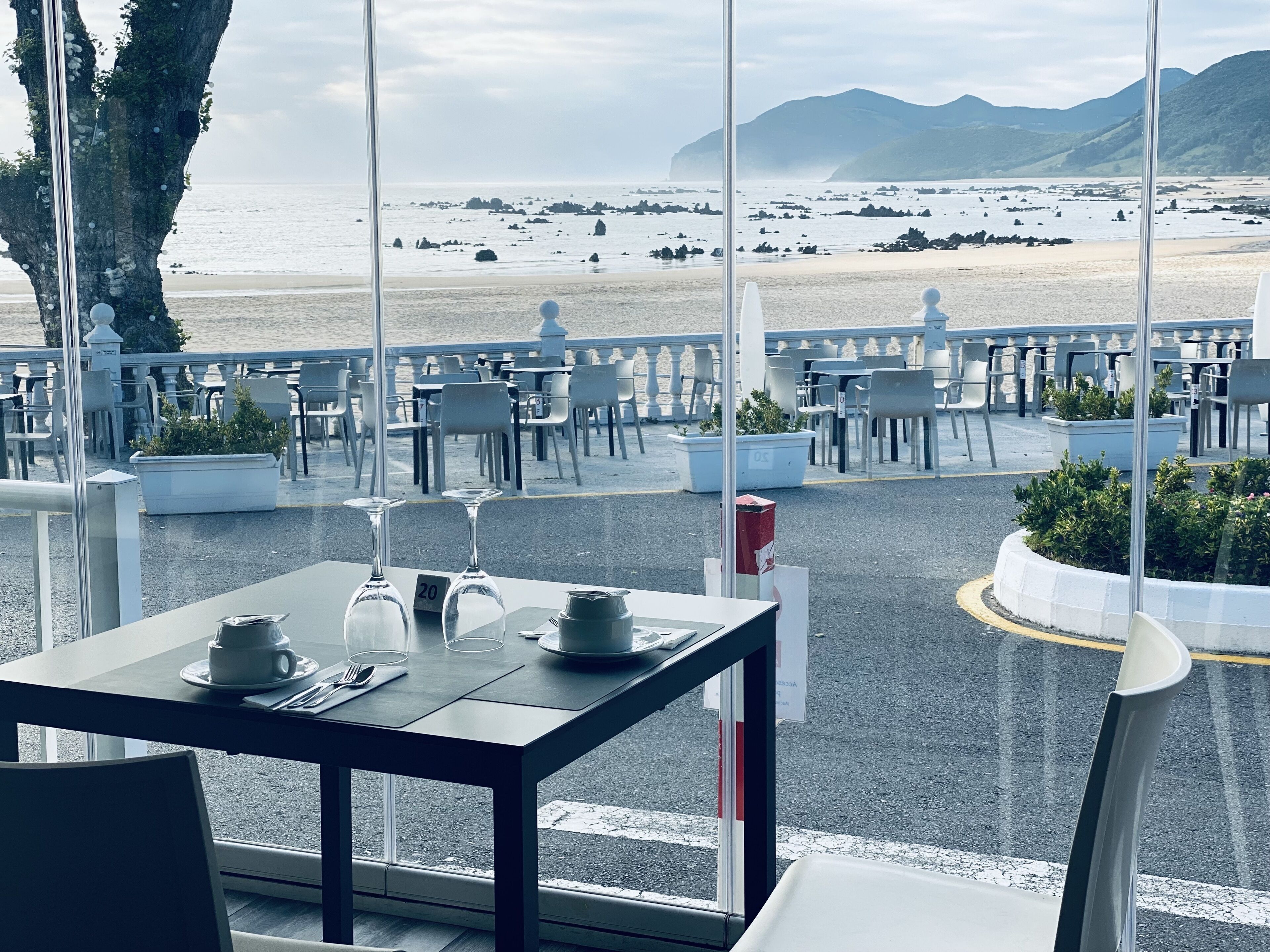 An outdoor dining area with tables and chairs, overlooking a beach and mountains.