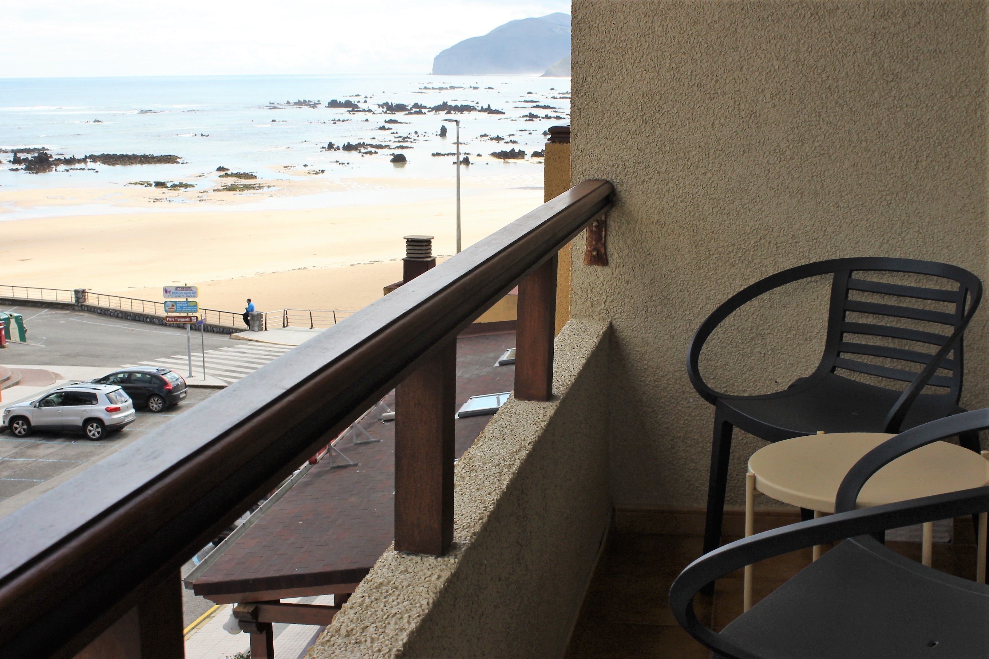 A balcony with a view of a beach, a table, and two chairs.
