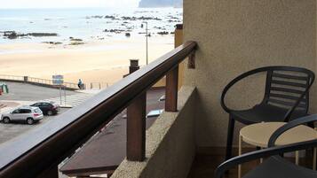 A balcony with a view of a beach, a table, and two chairs.