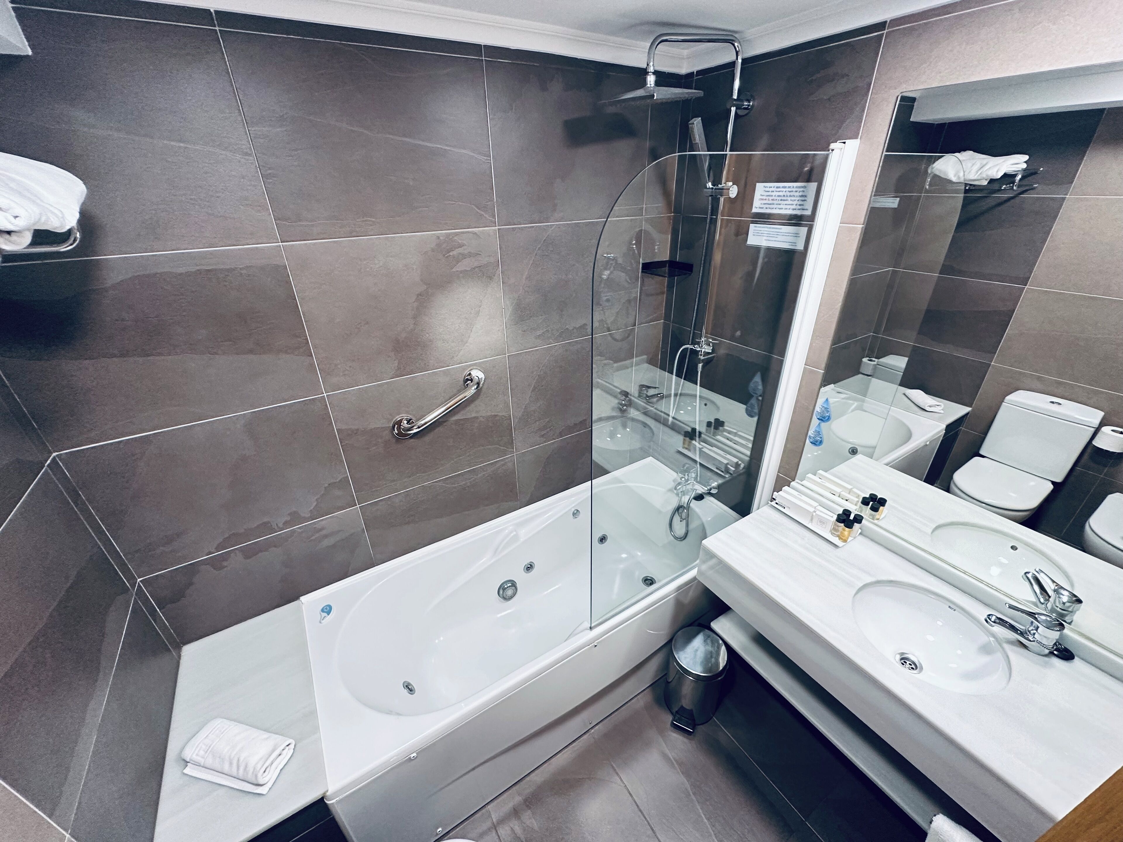 A modern bathroom with a glass-enclosed shower, a white bathtub, a sink, and a toilet.