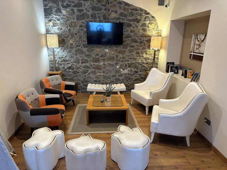 A living room with a stone wall, a flat-screen TV, white leather armchairs, a wooden coffee table, and a bookshelf with books.