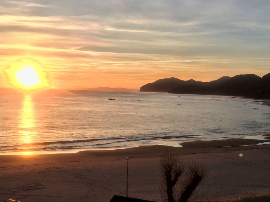 Una playa con un atardecer, mar tranquilo y montañas a lo lejos.
