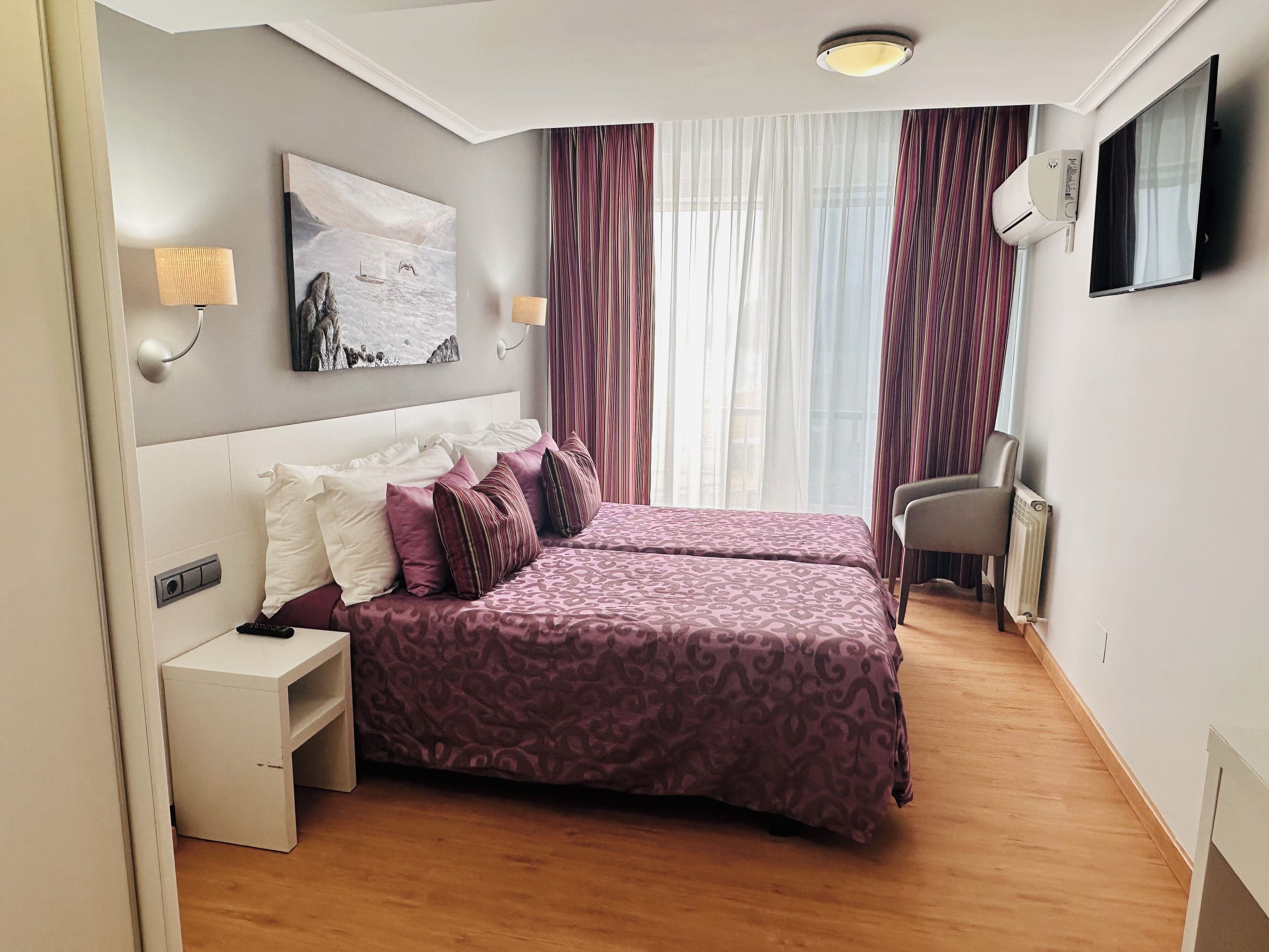 A hotel room with two beds, a desk, a chair, a TV, and a painting on the wall.