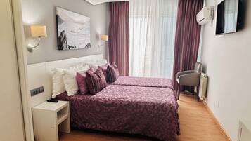 Habitación de hotel con dos camas, un escritorio, una silla, un televisor y un cuadro en la pared.