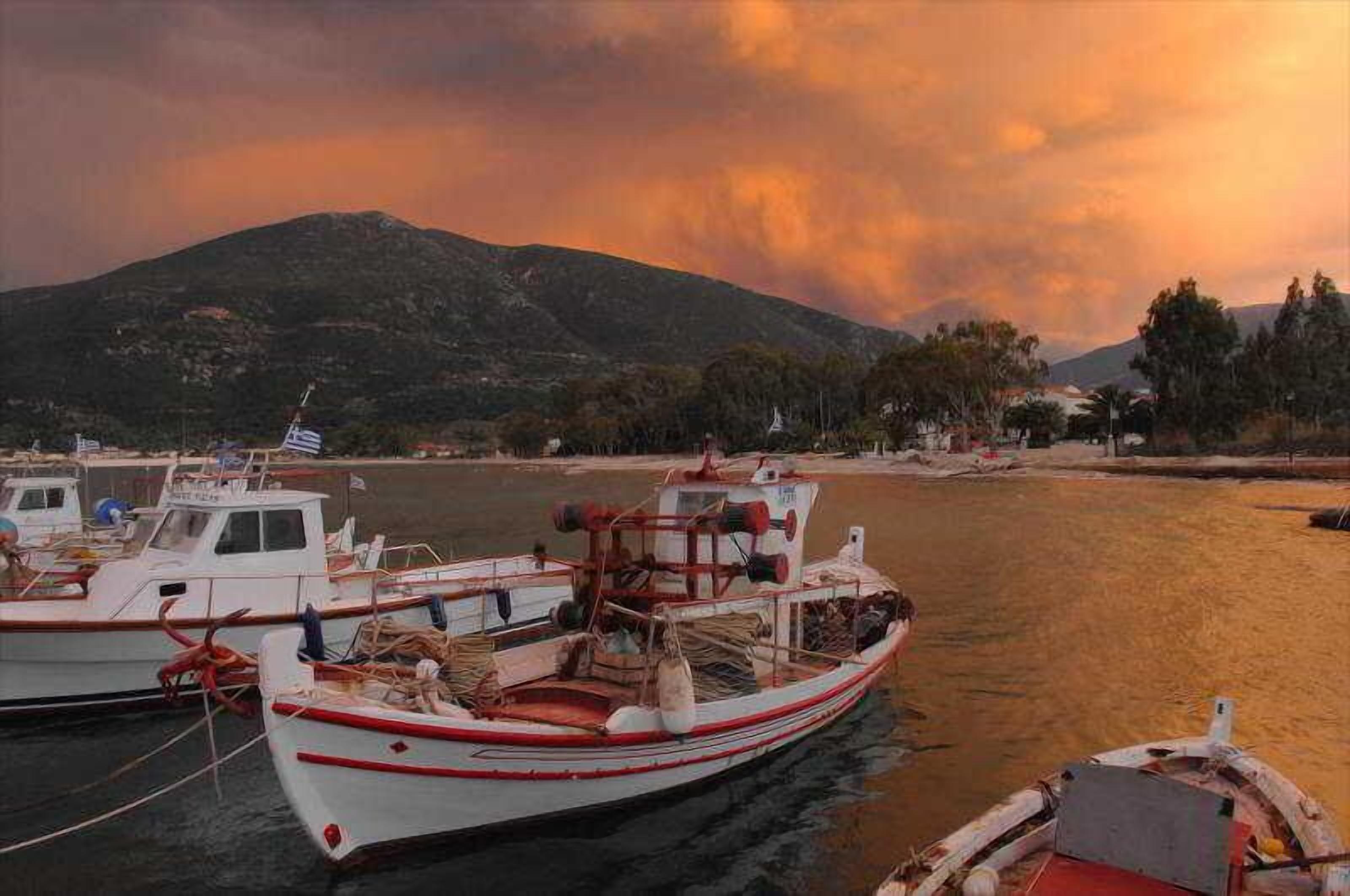 A harbor with boats docked, a mountainous backdrop, and a sandy beach.
