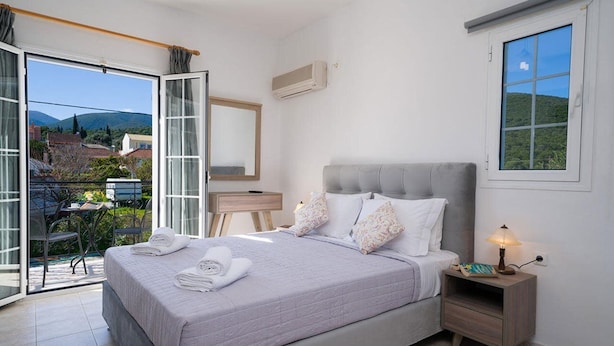 Une chambre à coucher avec un lit, une table de chevet, un miroir et une vue sur l’extérieur.