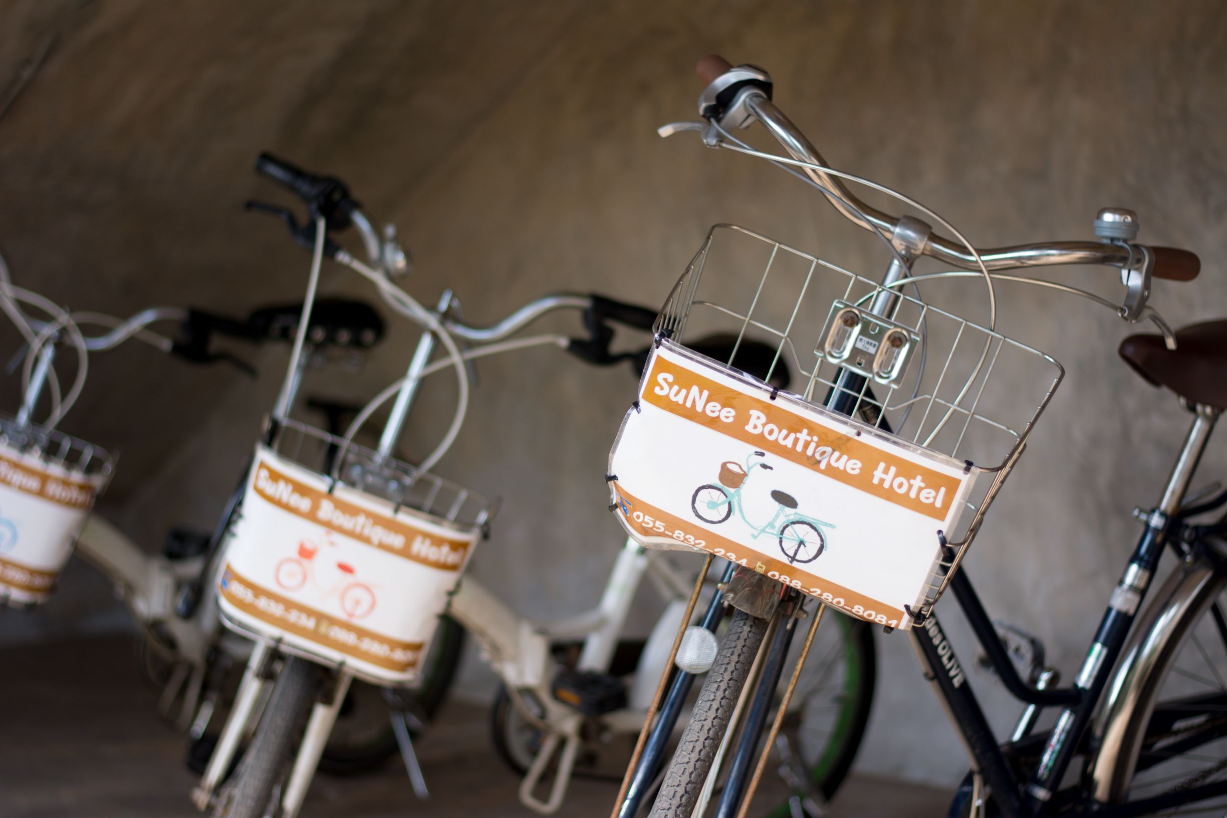A bicycle with a basket labeled "SuNee Boutique Hotel" and a phone number.
