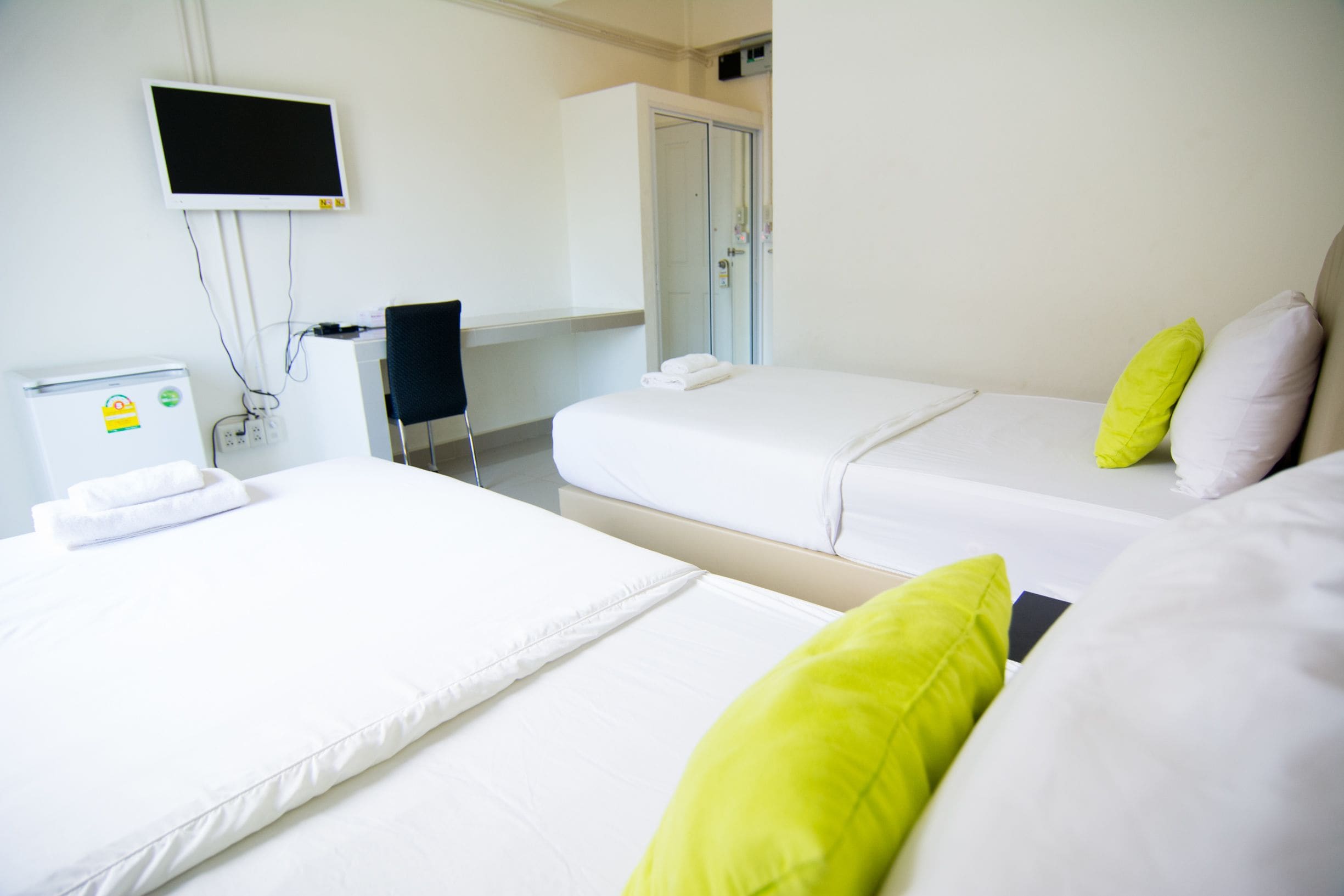 A hotel room with two beds, a TV mounted on the wall, a desk with a chair, and a wardrobe.