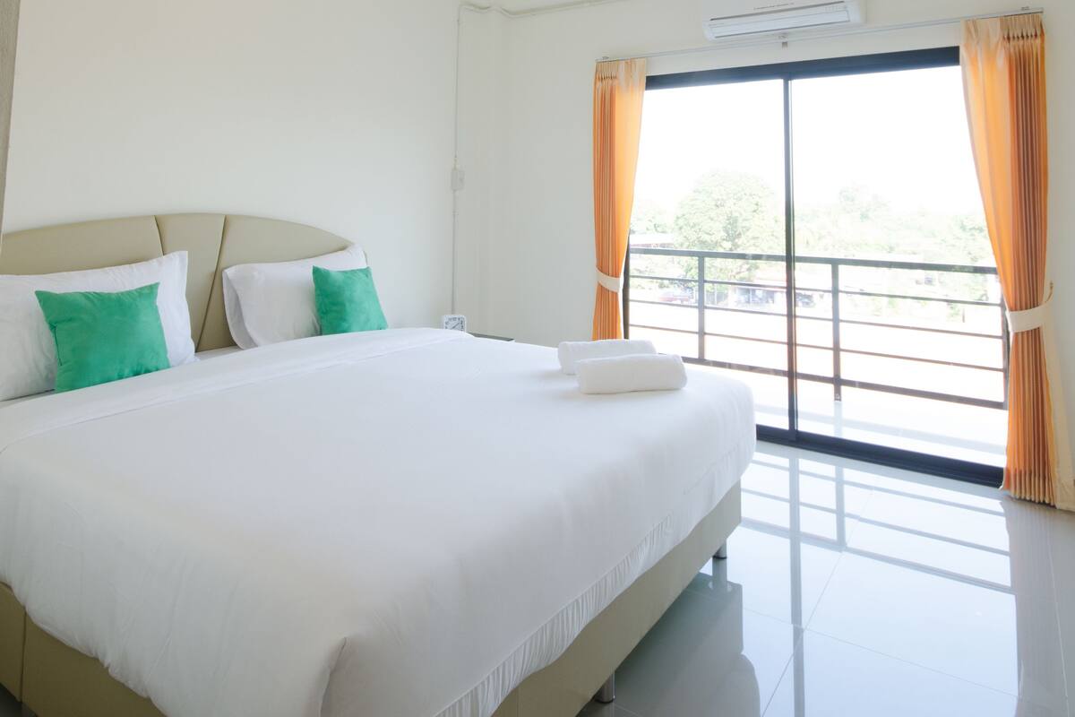 A hotel room with a large bed, a ceiling fan, an air conditioning unit, and a view of the outdoors through a sliding door.