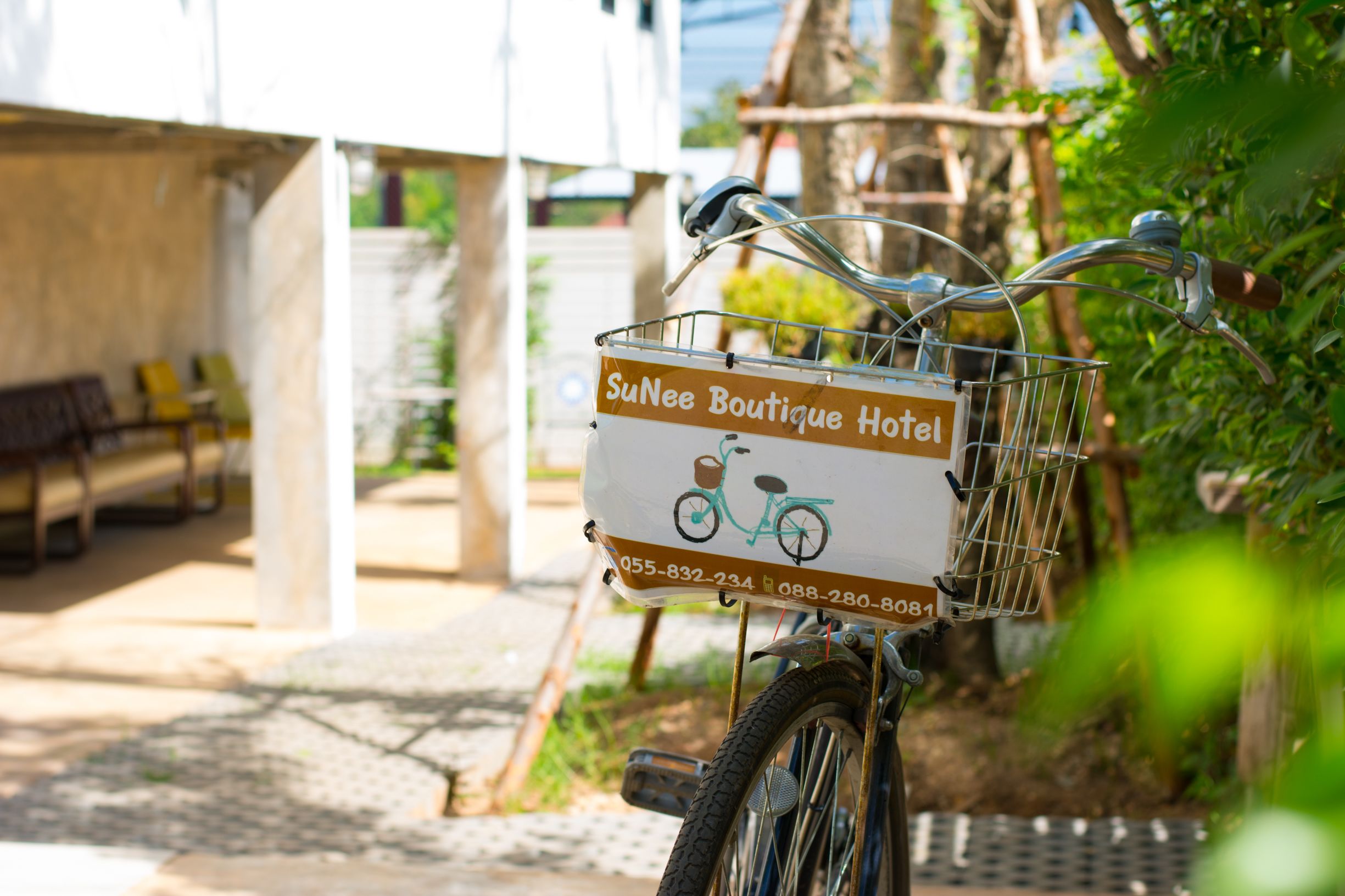 A bicycle with a basket labeled "SuNee Boutique Hotel" and contact numbers.