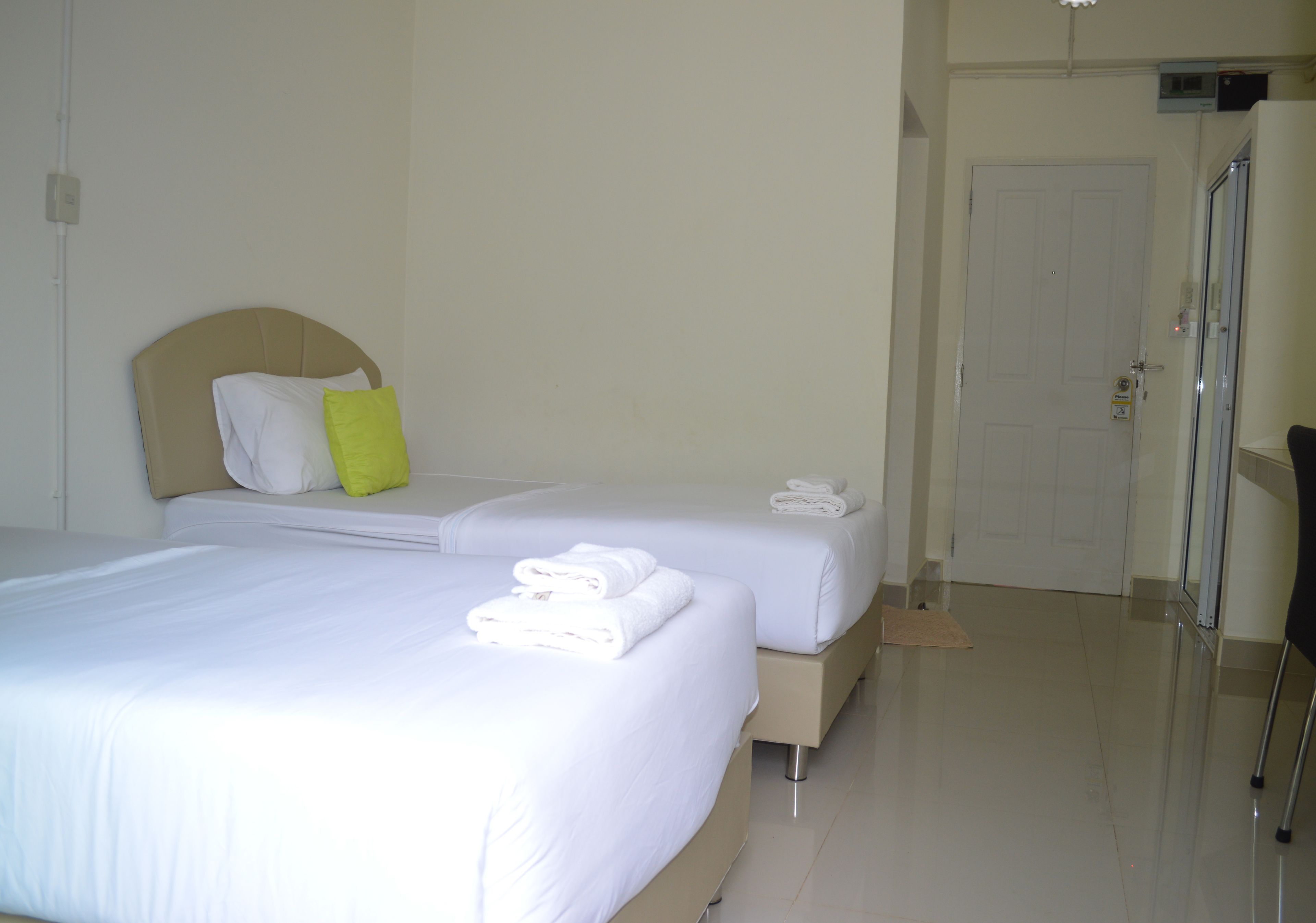 A hotel room with two beds, a white door, and a bathroom with a glass shower.