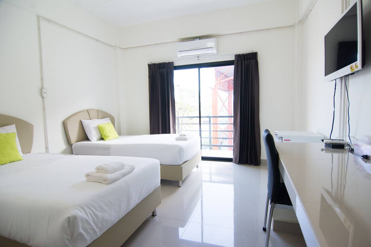 A hotel room with two beds, a desk, a chair, a TV, and an air conditioning unit.