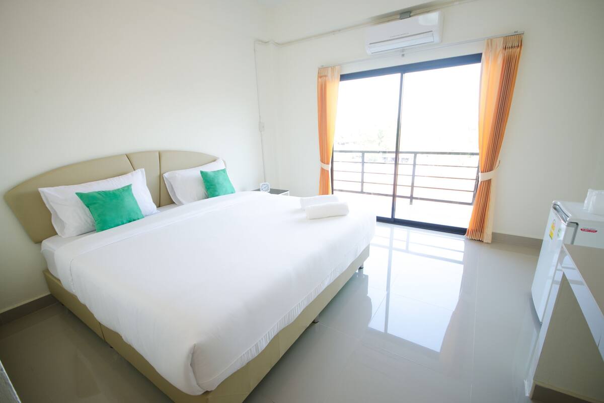 A hotel room with a bed, a desk, an air conditioner, and a view through the window.