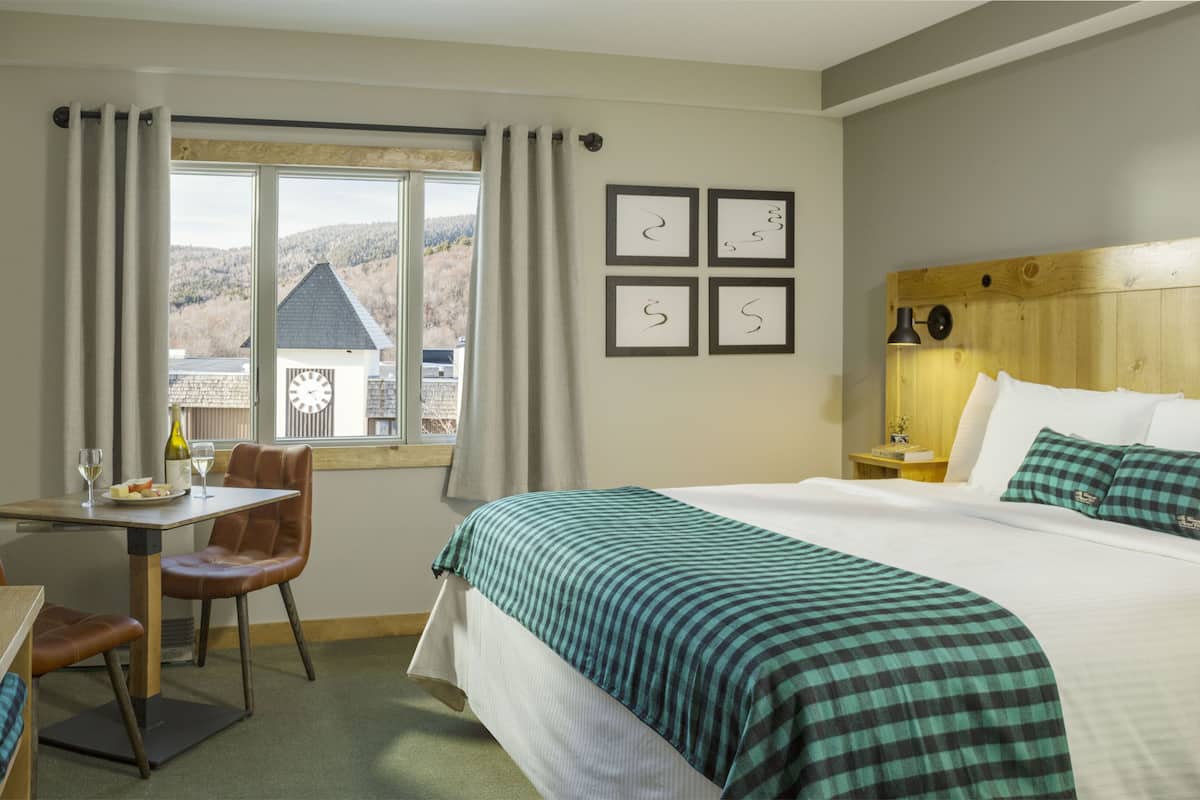 Ein Hotelzimmer mit Bett, Schreibtisch, Stuhl und Fenster mit Blick auf ein Haus und Hügel.