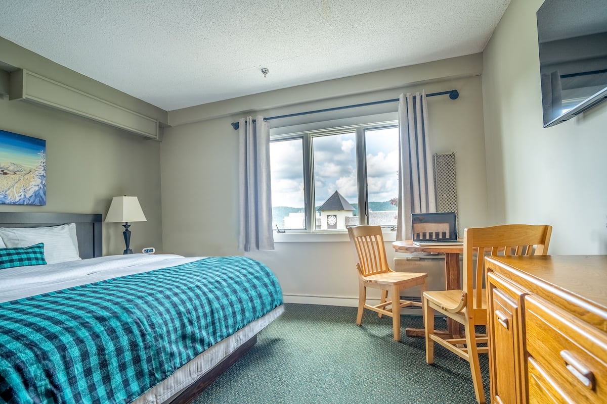 Ein Hotelzimmer mit Bett, Schreibtisch, Stühlen und Blick auf einen Glockenturm.