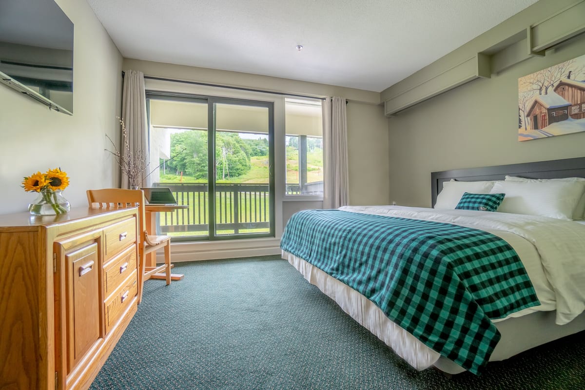 Ein Schlafzimmer mit Bett, Schminktisch, Sessel, Fenster mit Blick ins Grüne und einem Bild an der Wand.