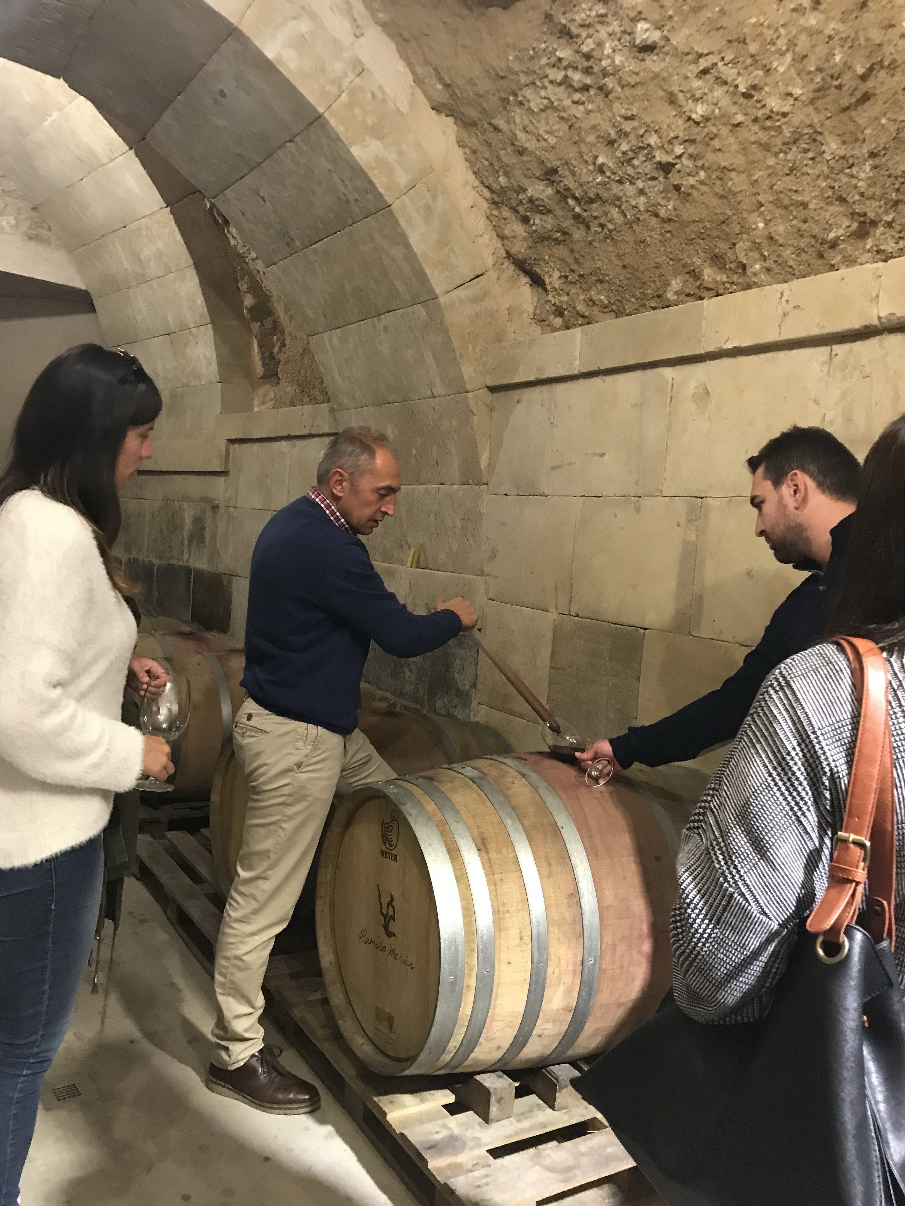A group of people interacting with large wooden barrels in a stone-walled room.
