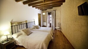 A bedroom with two beds, wooden beams on the ceiling, a nightstand with a lamp, and a chair. - Posada Real del Buen Camino (Villanueva de Campean)