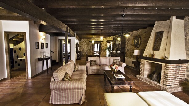 A spacious living room with striped sofas, a fireplace, and a stone wall. - Posada Real del Buen Camino (Villanueva de Campean)